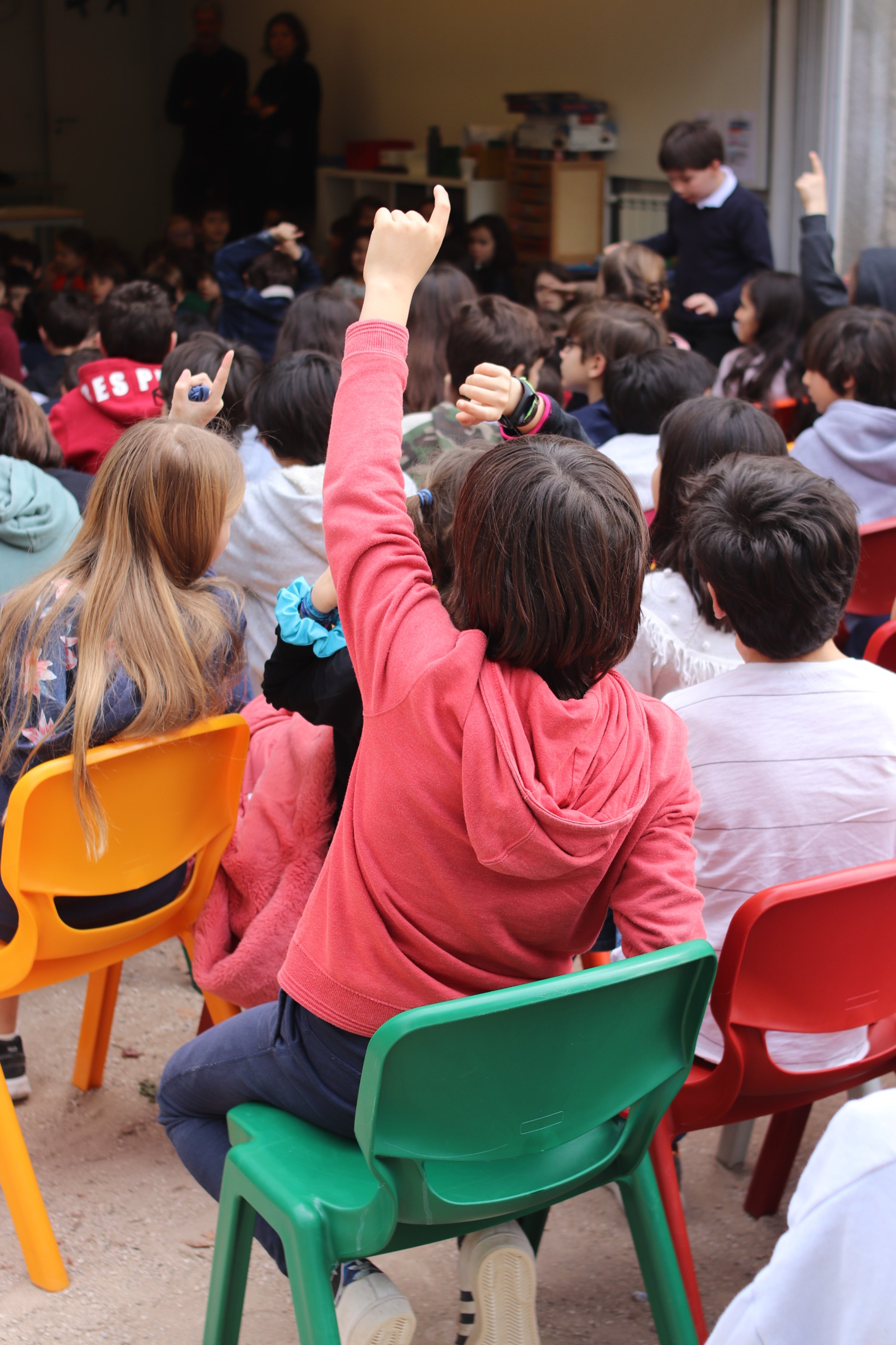 Preschool children actively participating in a classroom activity, raising their hands to answer questions or share ideas.