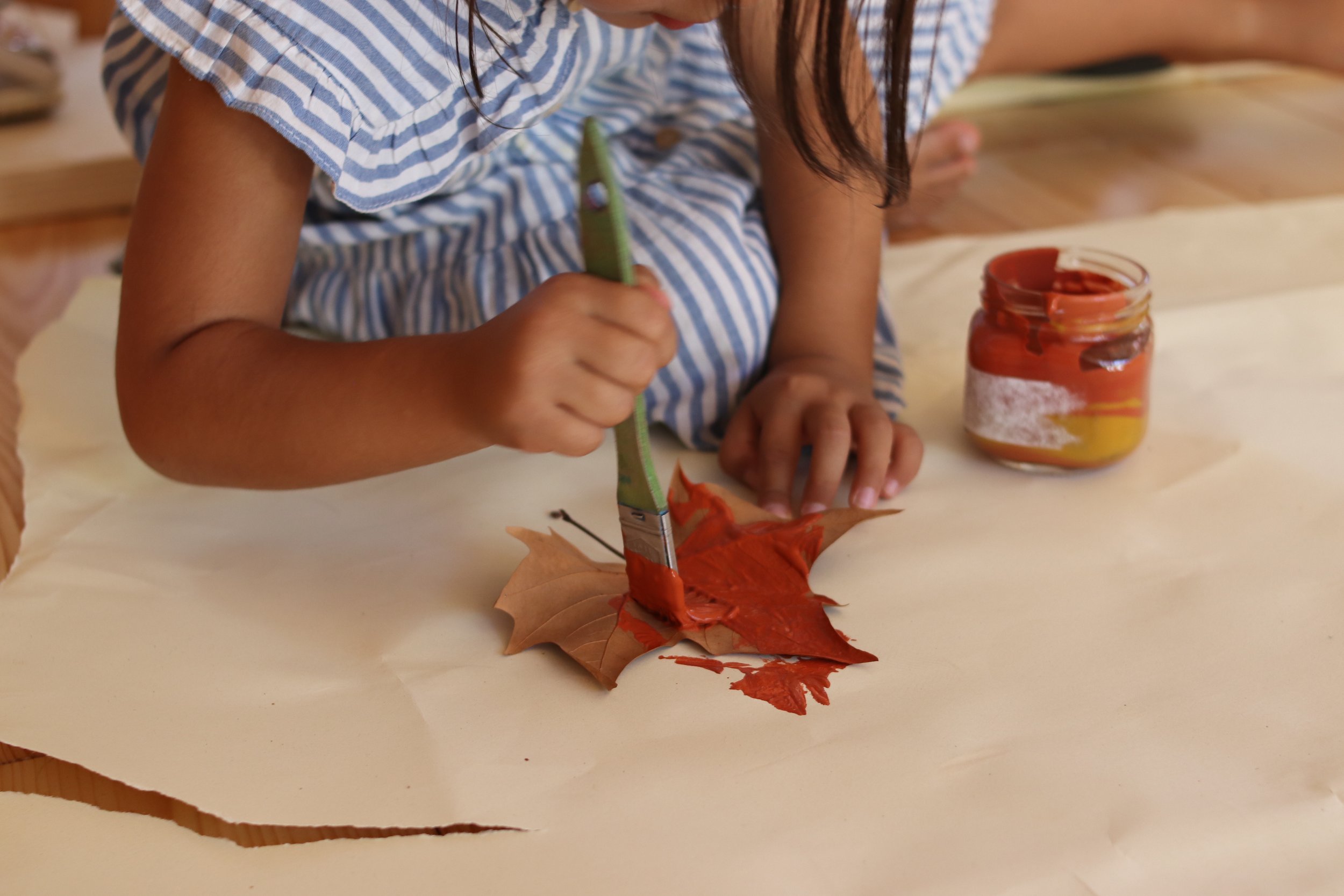 Preschool child painting a leaf with orange paint