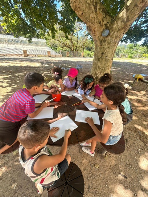 Preschool children drawing and painting outdoors under a tree