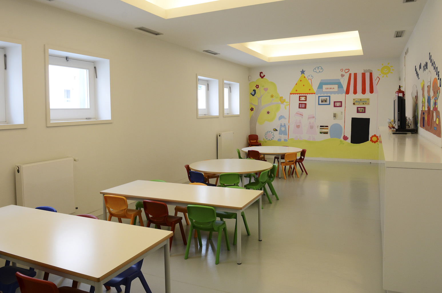 Preschool classroom with colorful tables and chairs, and a mural on the wall