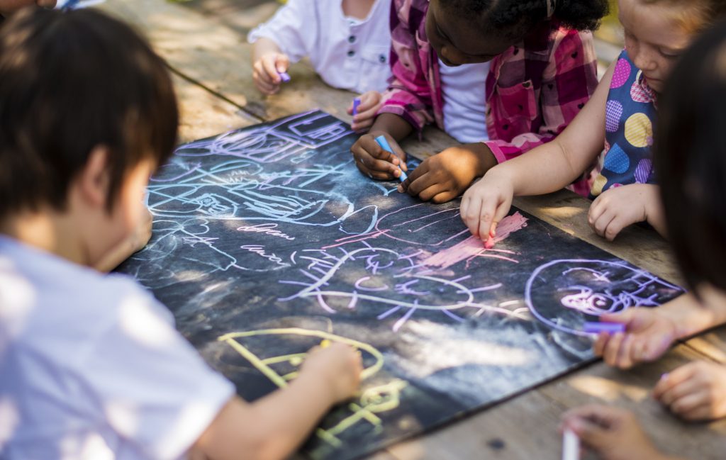 Preschool children drawing with chalk on a large chalkboard outdoors