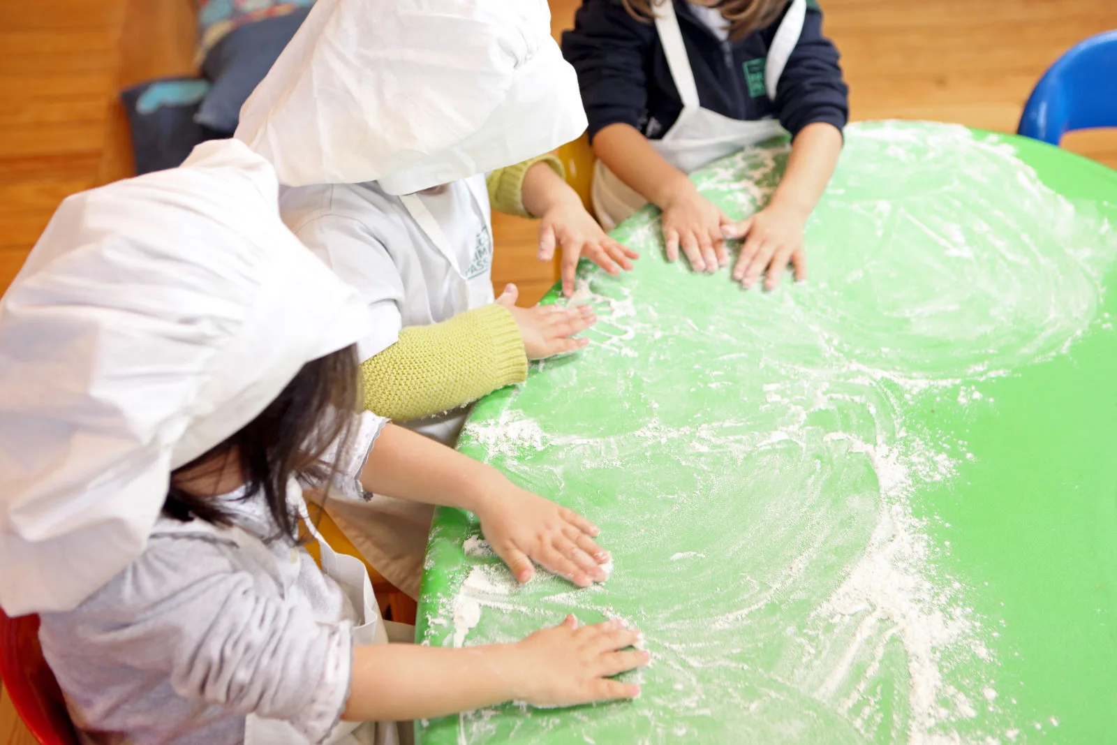 Preschool children in chef hats playing with flour on a green table