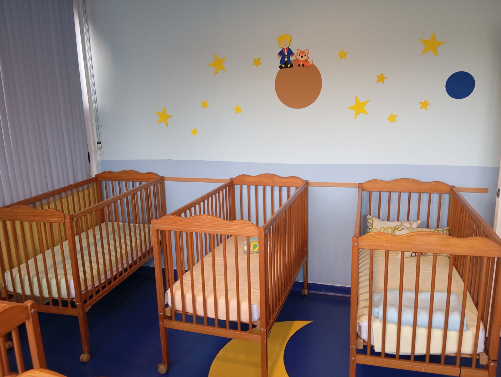 Preschool nap room with Little Prince themed decor and wooden cribs