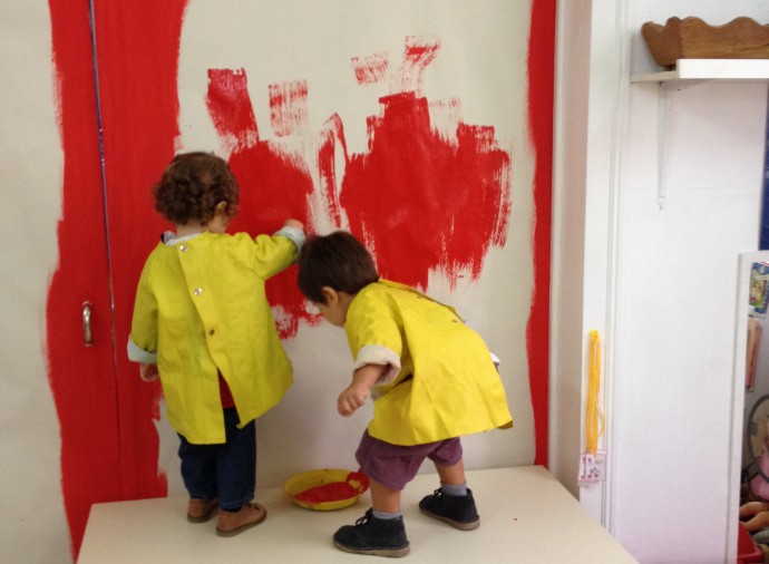 Two preschool children painting a wall red