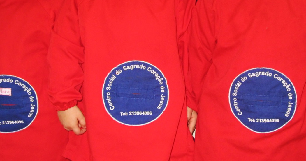 Back view of three children wearing red uniforms with the school logo embroidered on them.