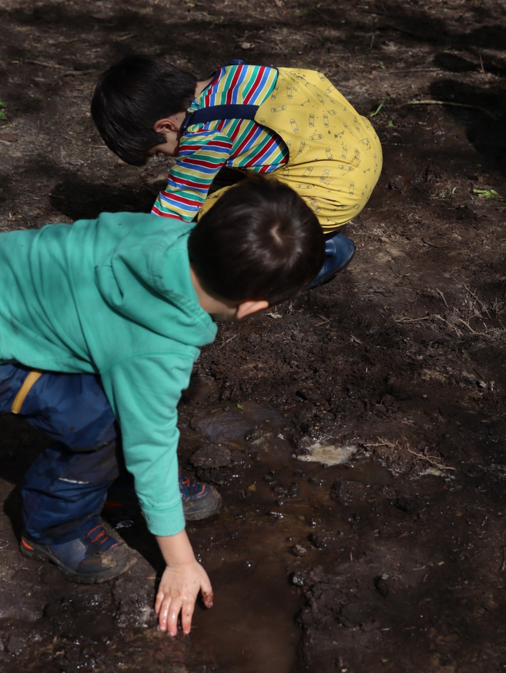Two preschool children playing in a mud puddle