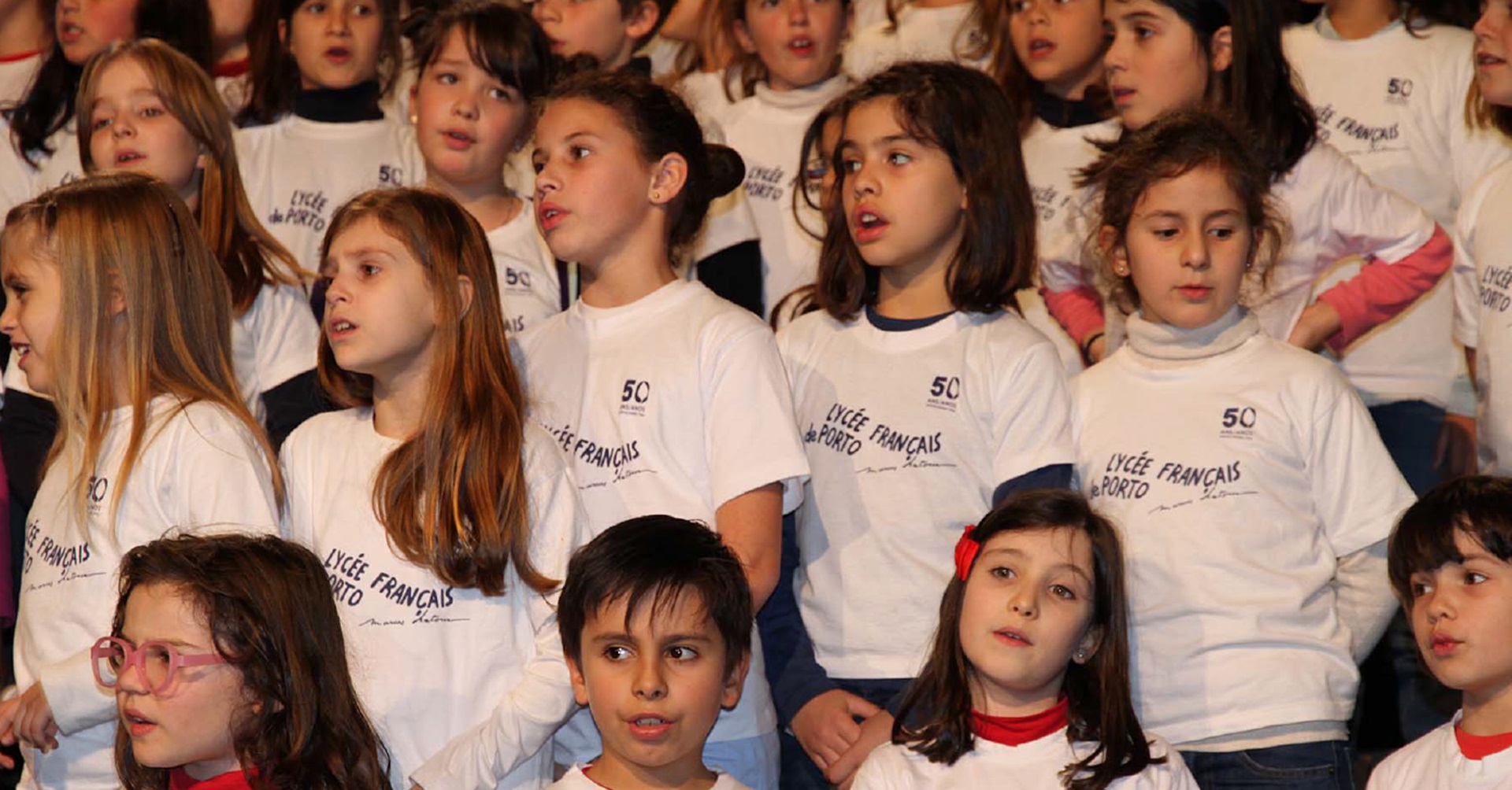Group of children in white shirts with the school logo singing