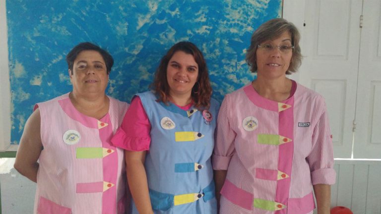 Three teachers at Os Cartolinhas preschool in matching uniforms.