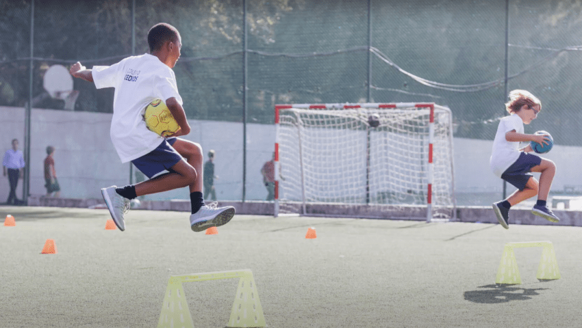 Two students joyfully jumping over hurdles during a soccer practice at Colégio Cedros.