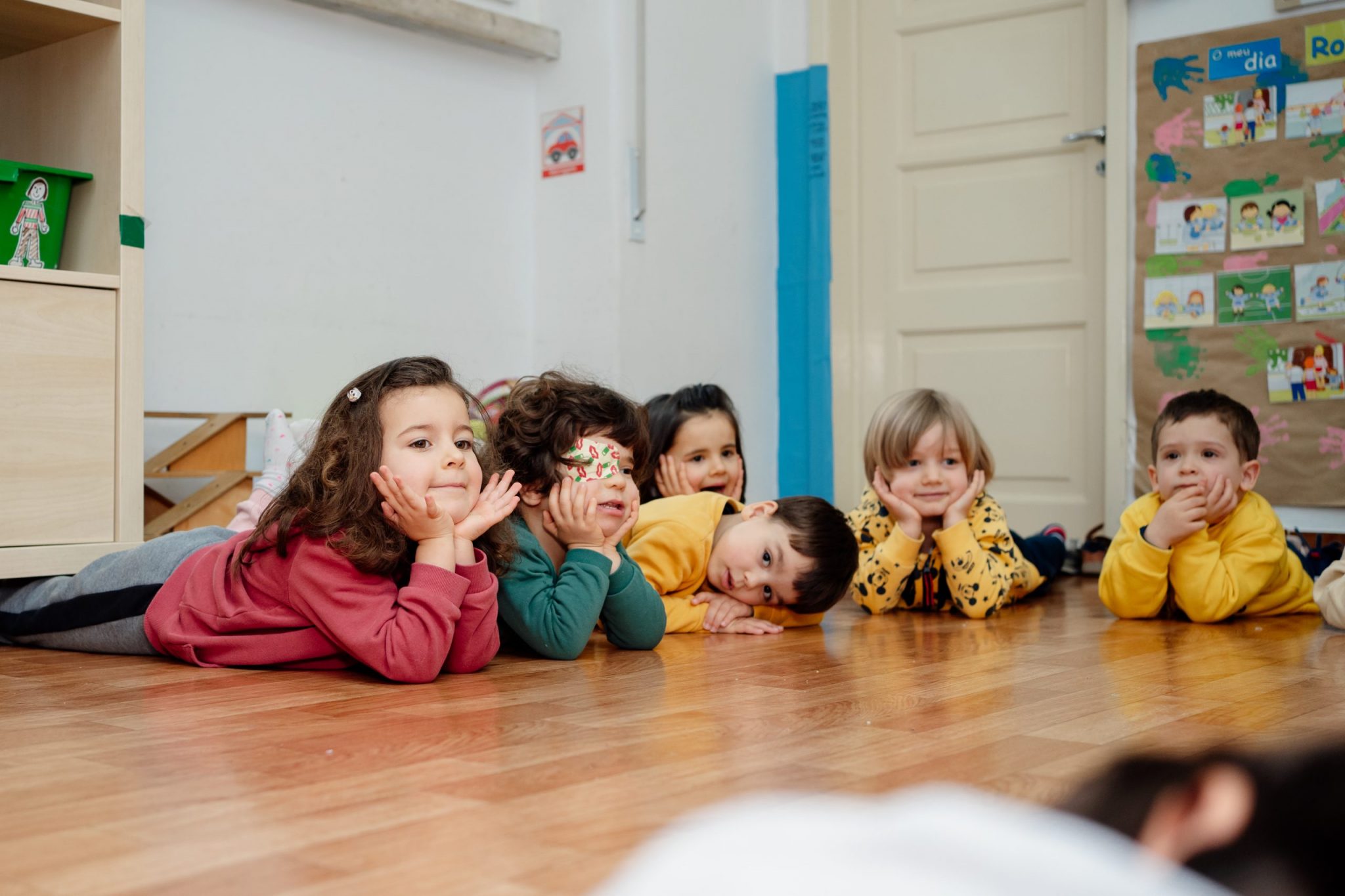 Preschool children lying on the floor, participating in a classroom activity.