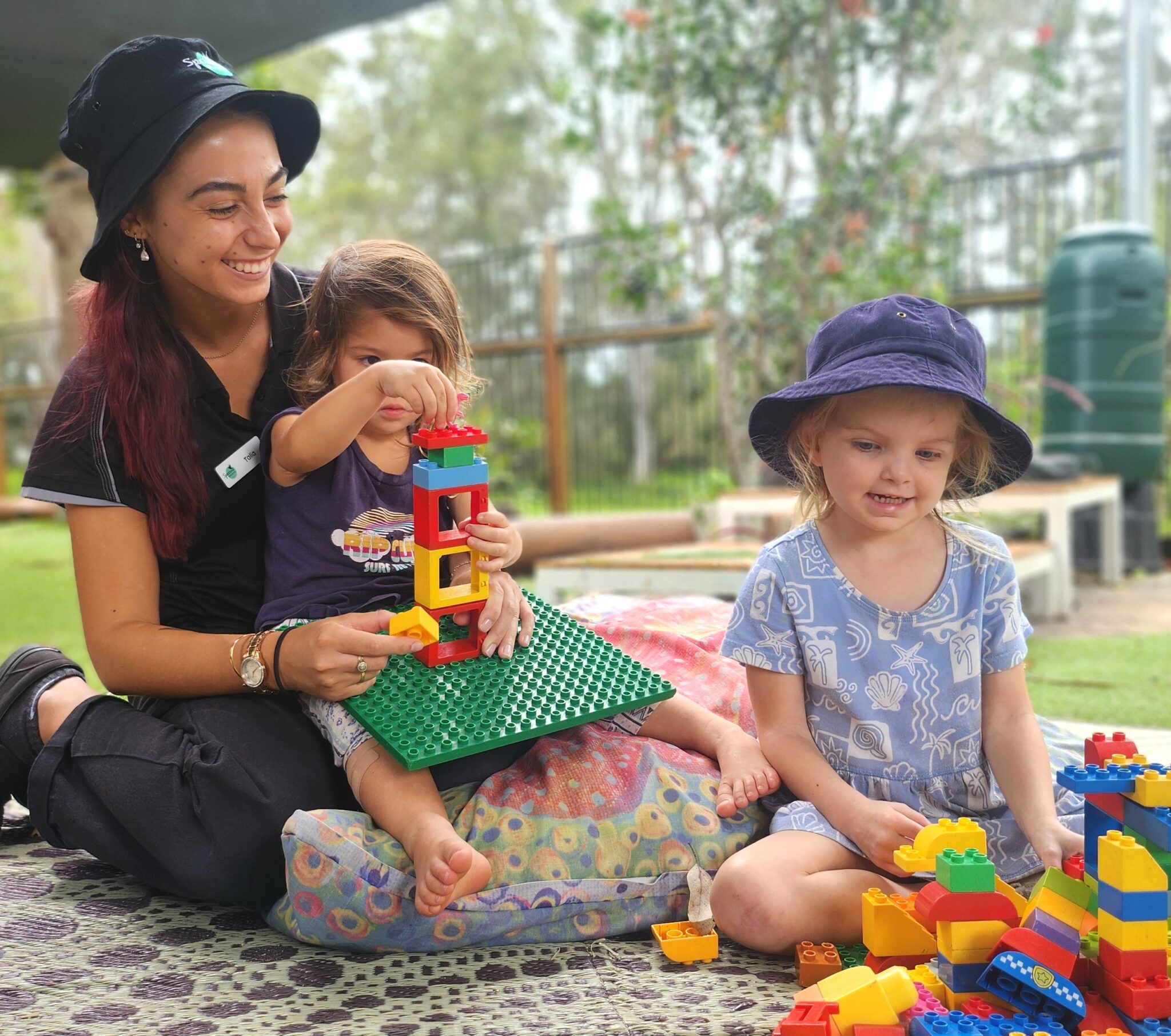 Preschool teacher assisting children with Lego blocks during outdoor playtime