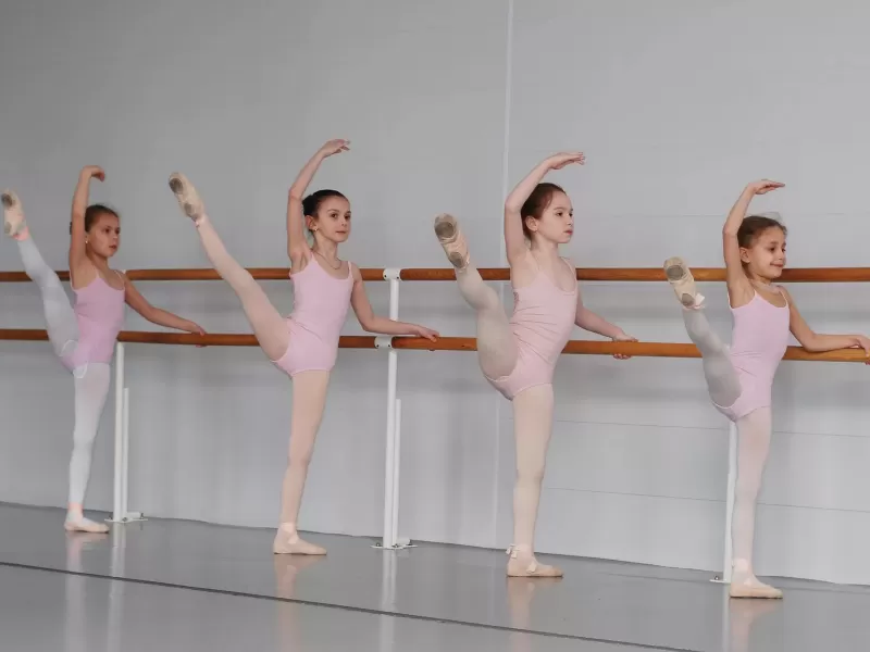 Four young ballerinas in pink leotards practicing at a barre