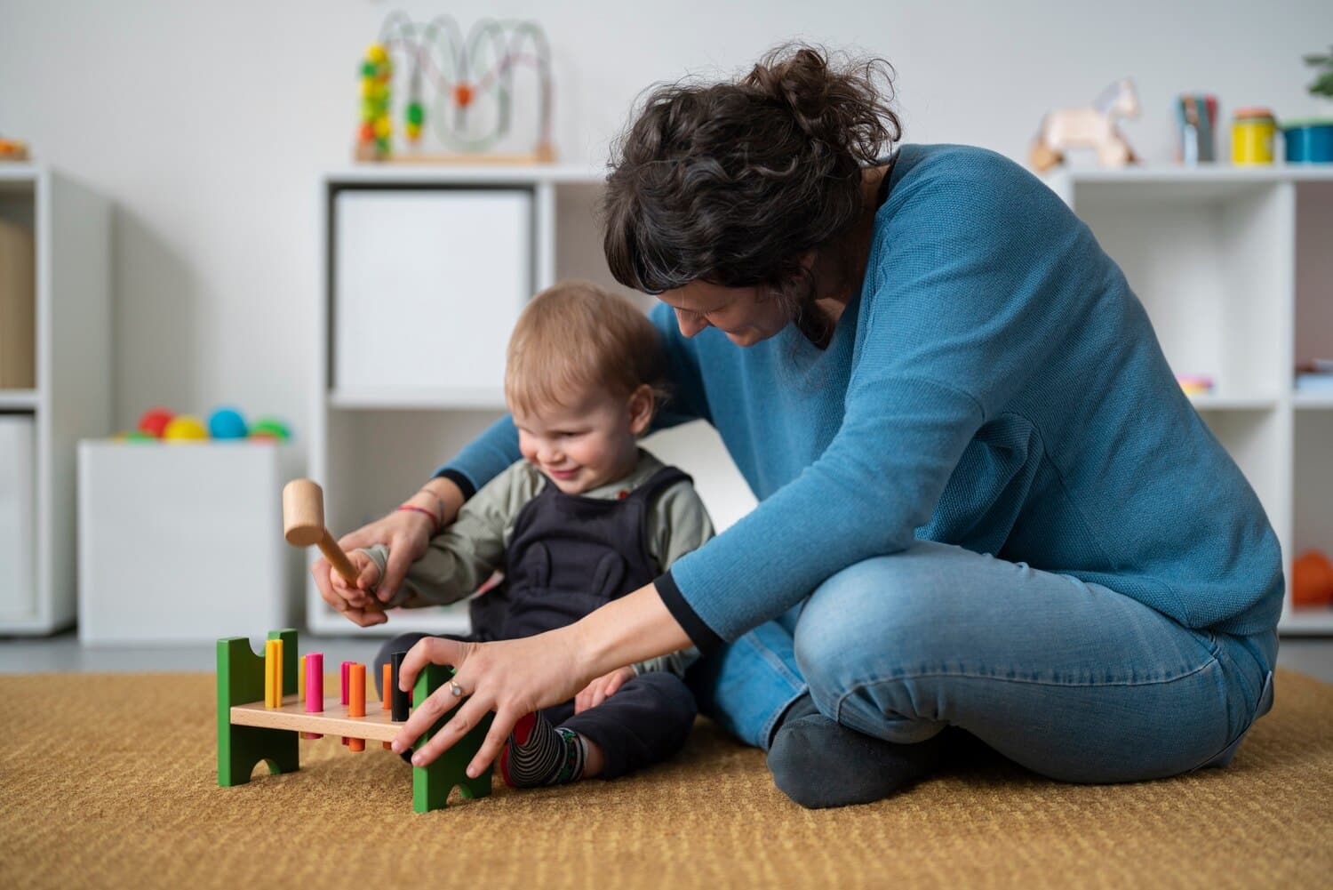 Preschool teacher assisting a toddler with a hammer and peg toy