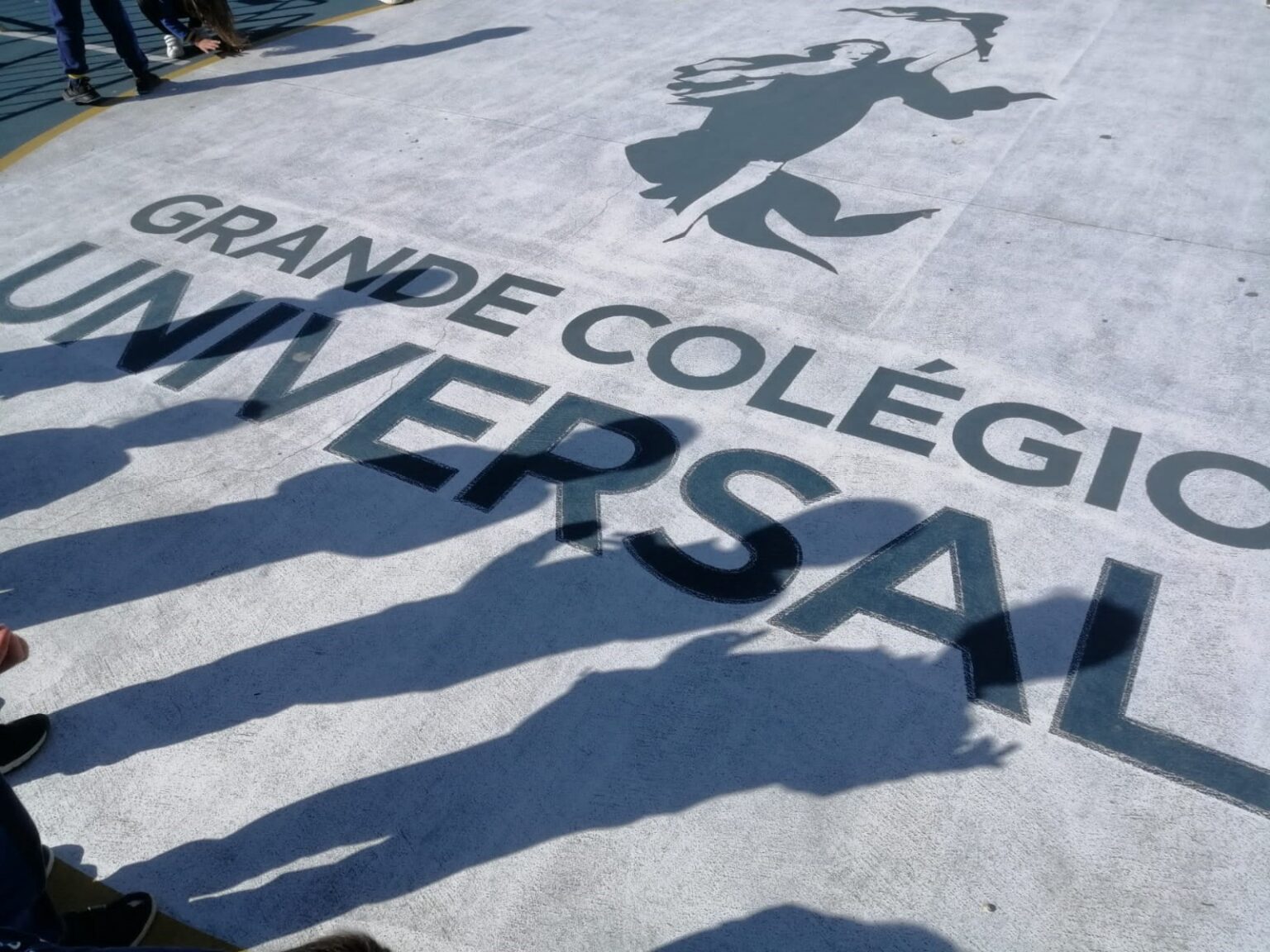 Shadows of students standing over the school's name, Grande Colegio Universal, painted on the ground.