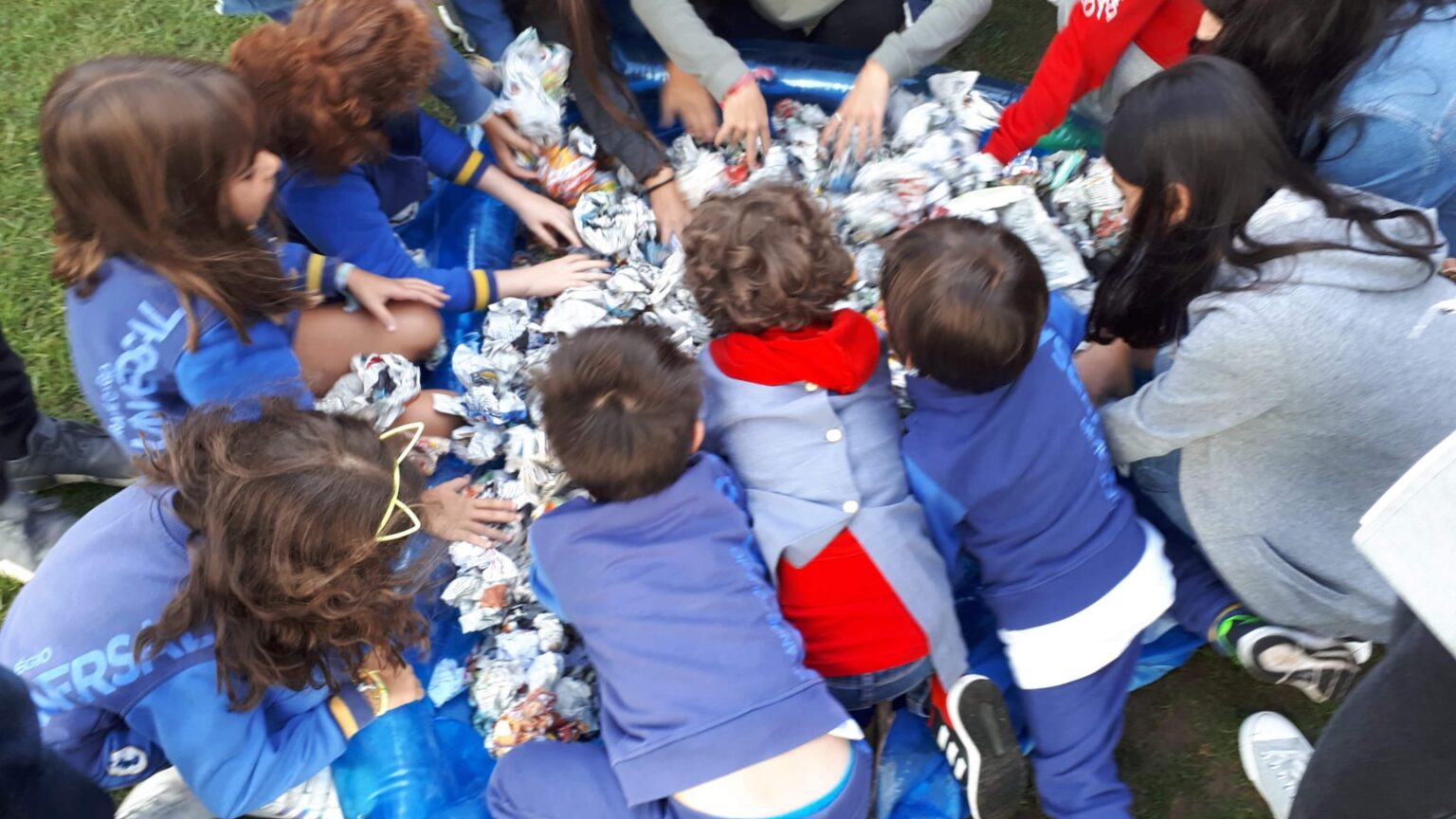 Preschool children participating in a group activity, surrounding a pile of crumpled paper.