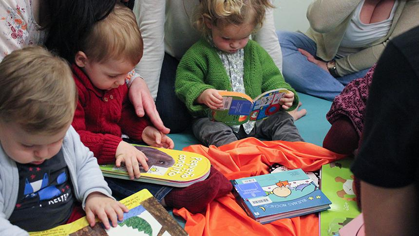 Preschool children sitting on the floor and reading books with their teachers