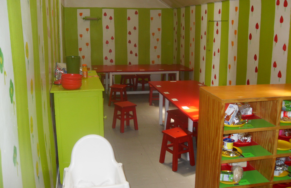 Preschool classroom with red tables and chairs, and green and white striped walls decorated with flower patterns.