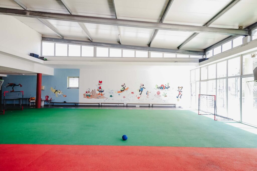 Preschool gymnasium with green and red floor, wall mural, and soccer goal