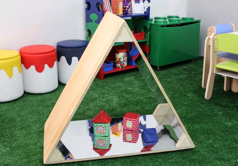 Wooden triangular mirror in a preschool classroom, reflecting colorful blocks and toys