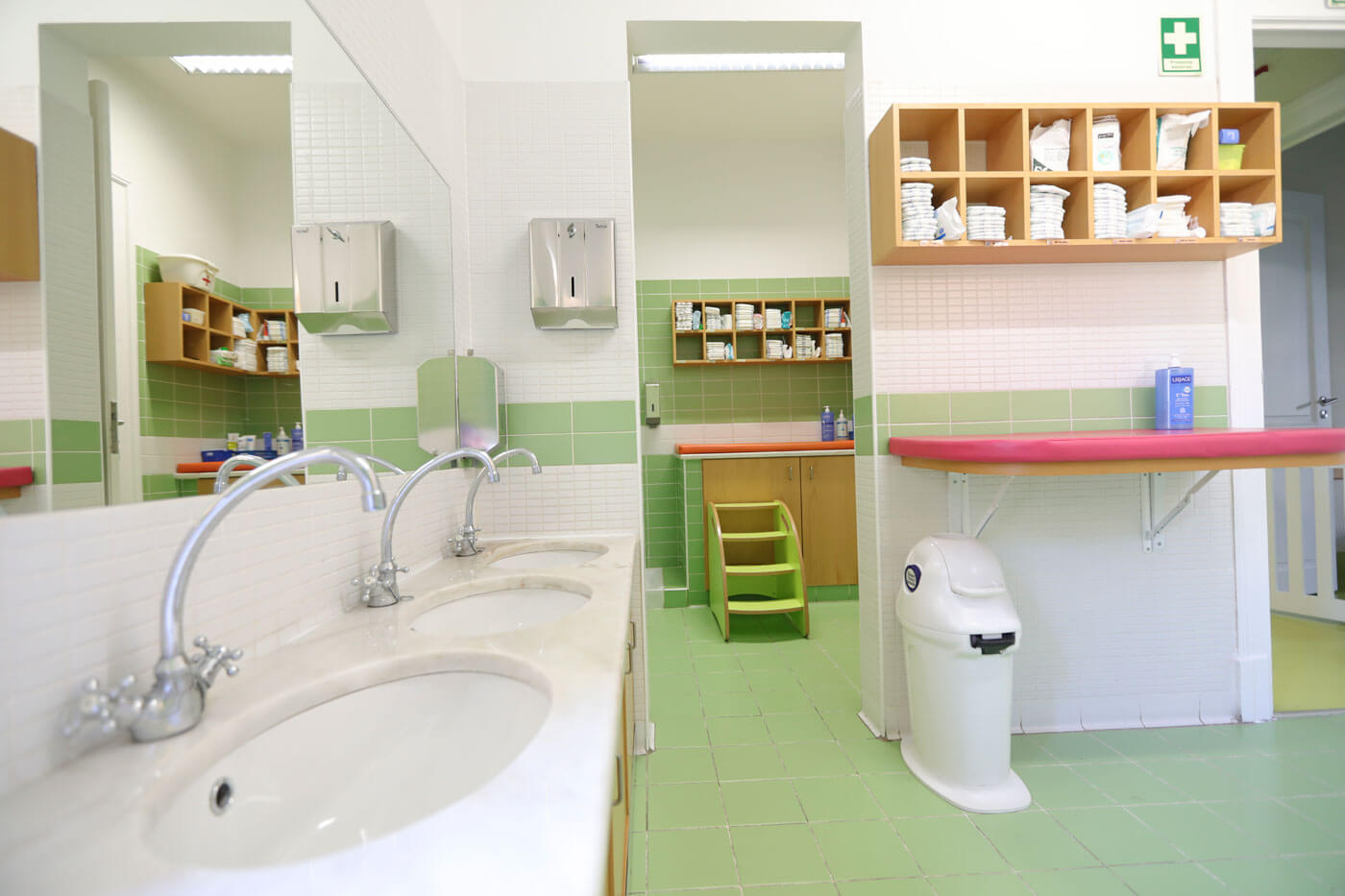 Preschool bathroom with sinks, changing table, and shelves stocked with supplies