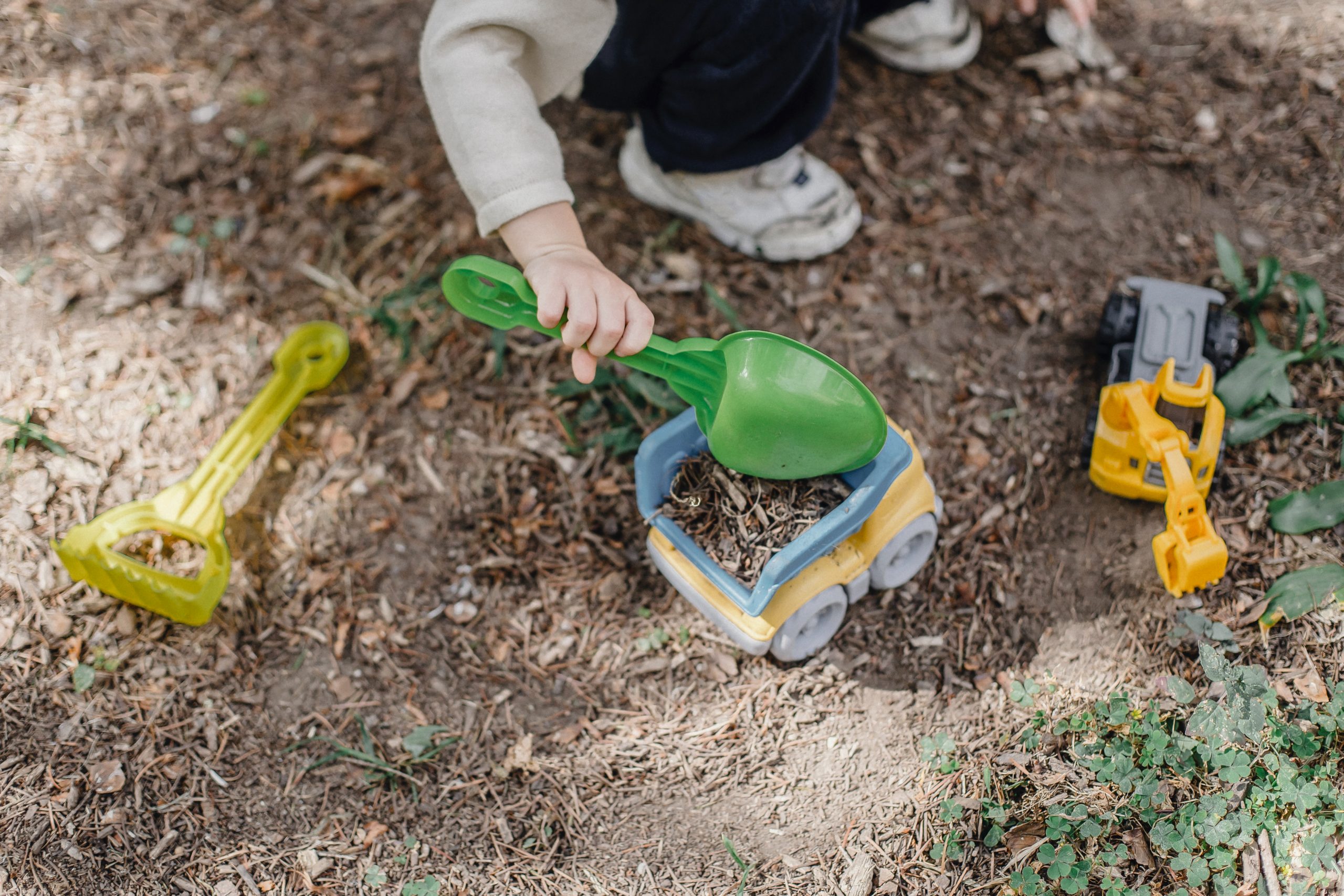Preschool child playing with toy trucks and shovels outdoors