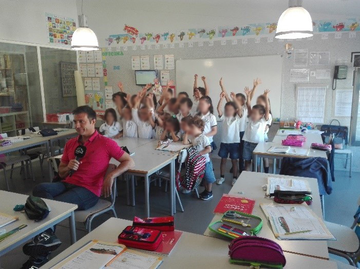 Preschool classroom with children raising their hands and a man holding a microphone