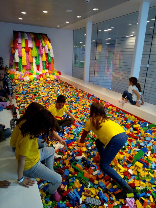 Preschool children playing with Lego blocks in a large indoor play area.