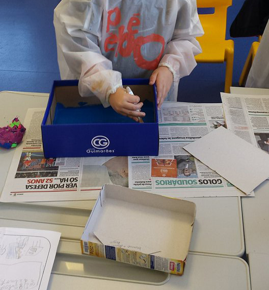 Preschool child painting a blue surface inside a box during an art class.