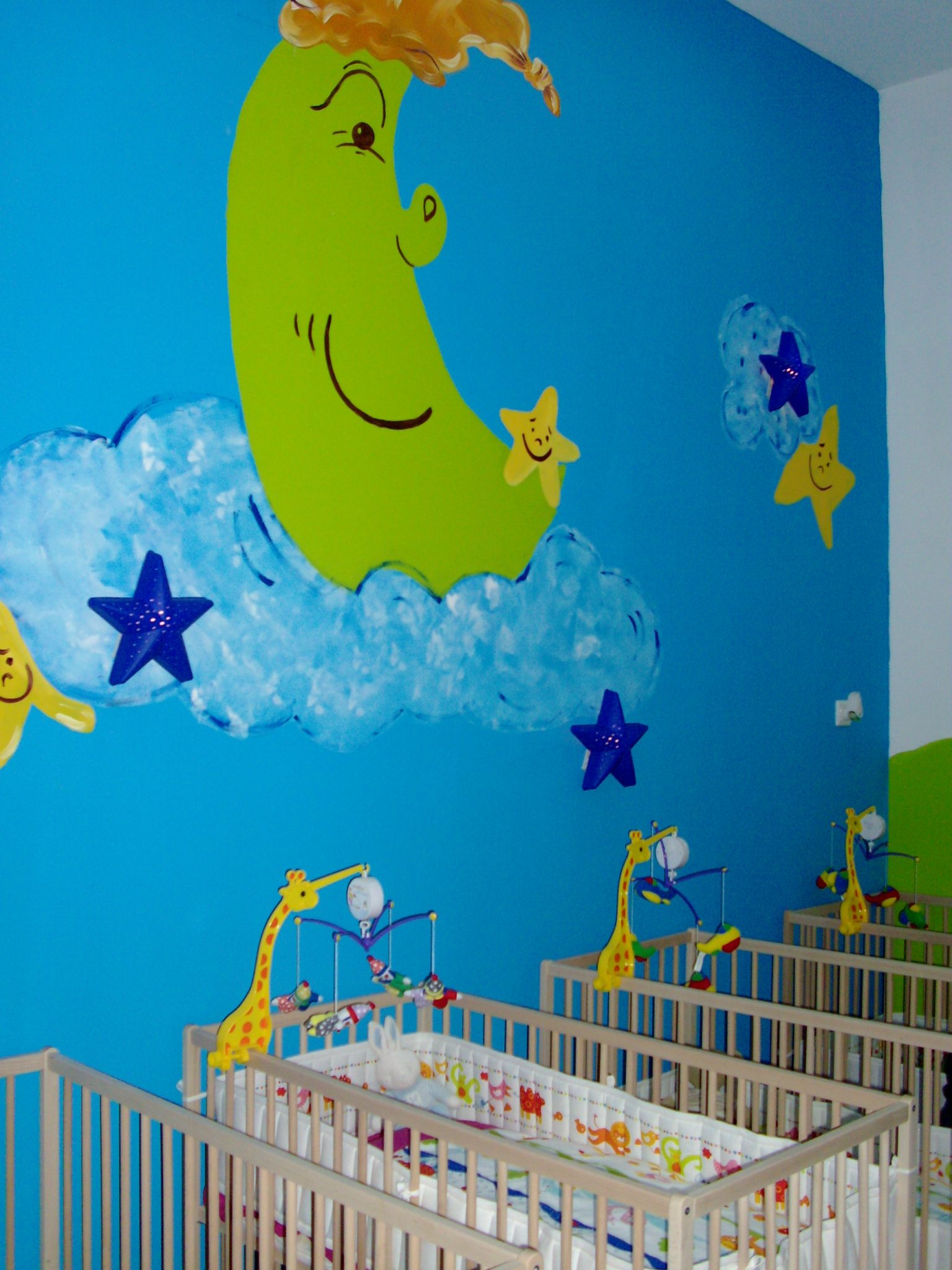 Nursery room with cribs and a moon and stars mural