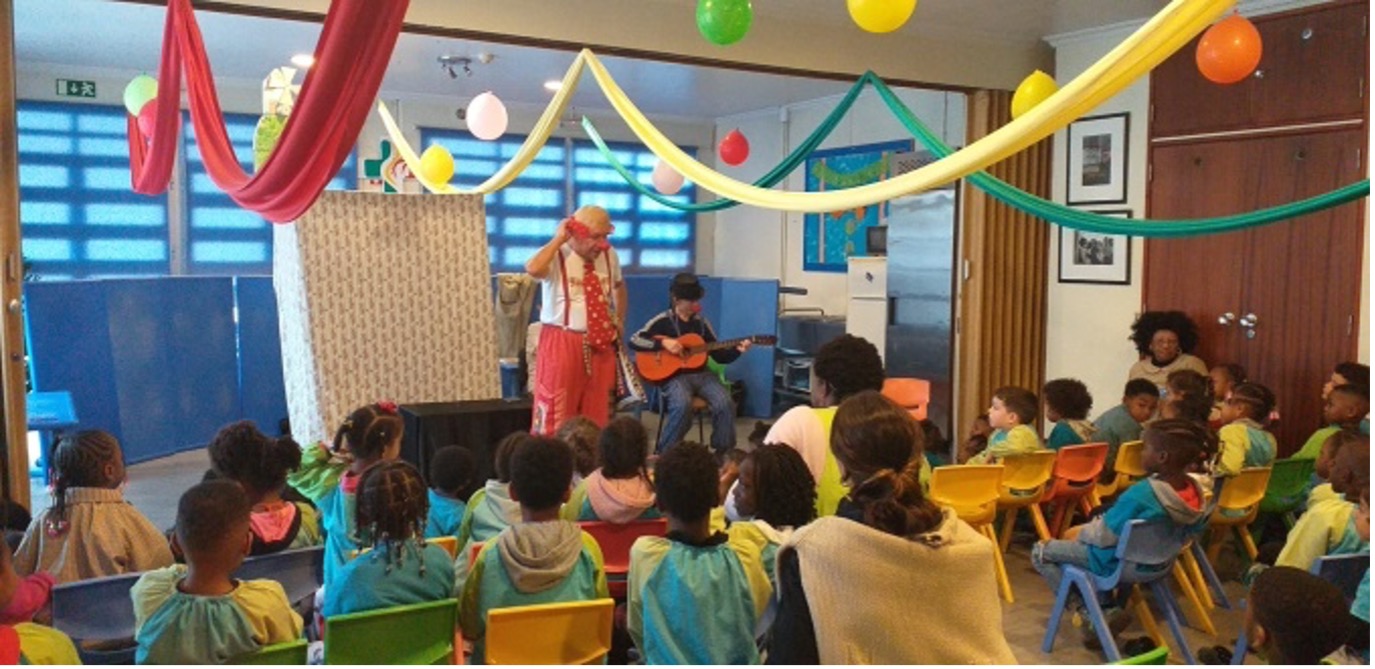 Preschool children enjoying a musical performance by a clown and a guitarist