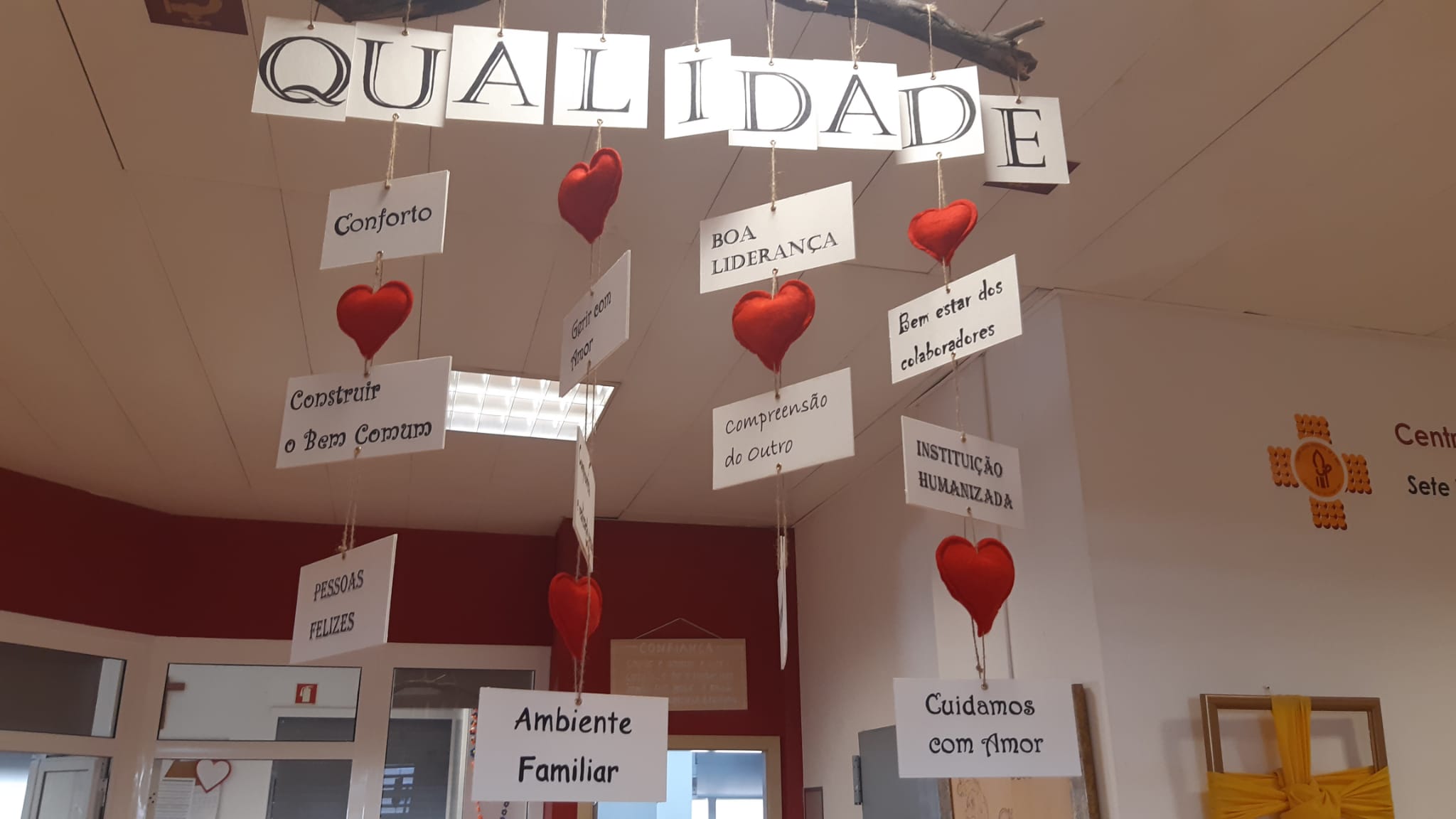 Interior view of Parish Social Center of S. Brás, showing a classroom decoration with the word "QUALIDADE" (quality) and several hanging hearts and signs with words emphasizing values like comfort, good leadership, and a humanized institution.