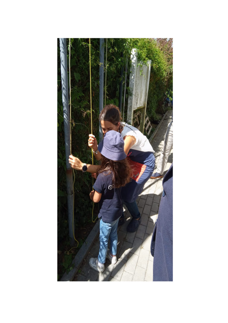 Preschool teacher assisting a child with an outdoor activity involving ropes and poles.