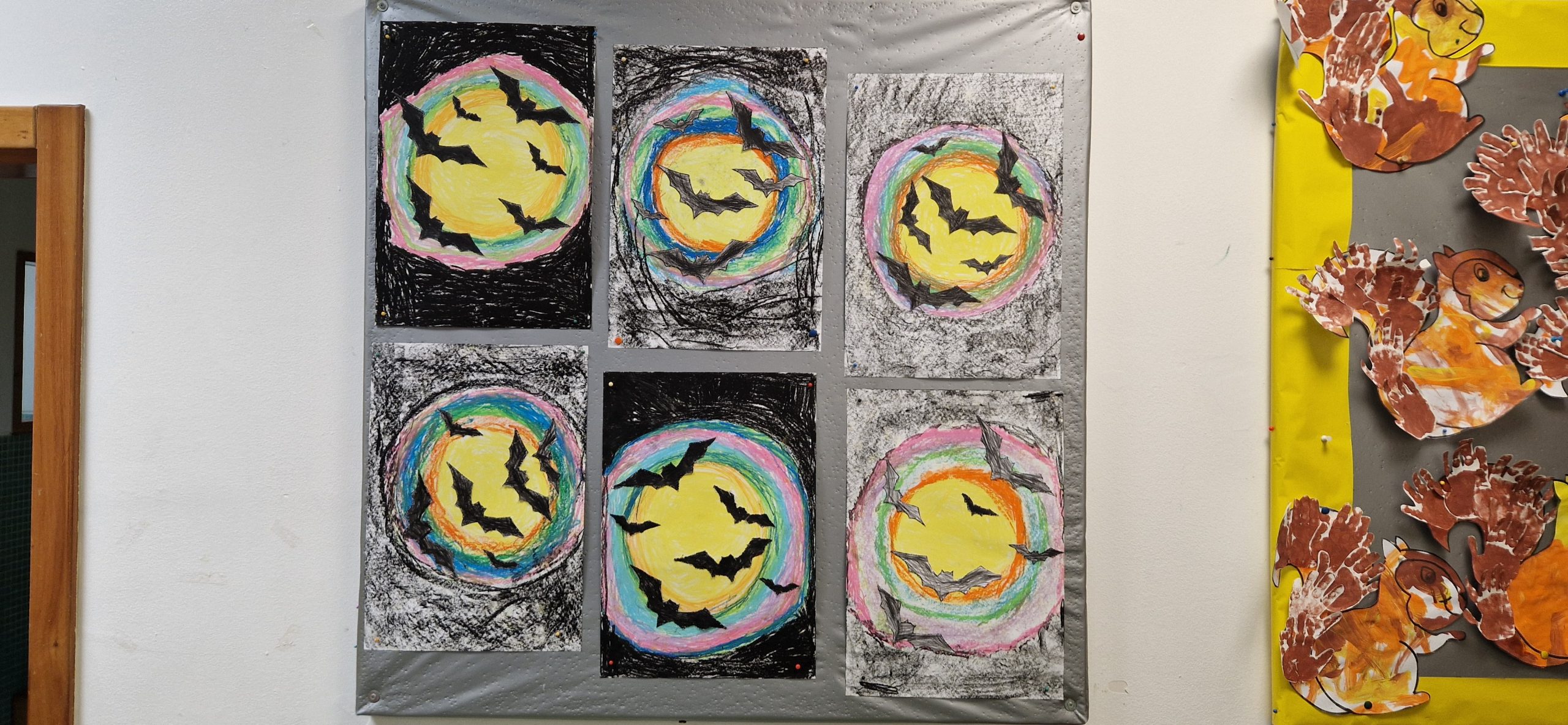 Preschool children's artwork featuring bats and a rainbow moon, displayed on a wall