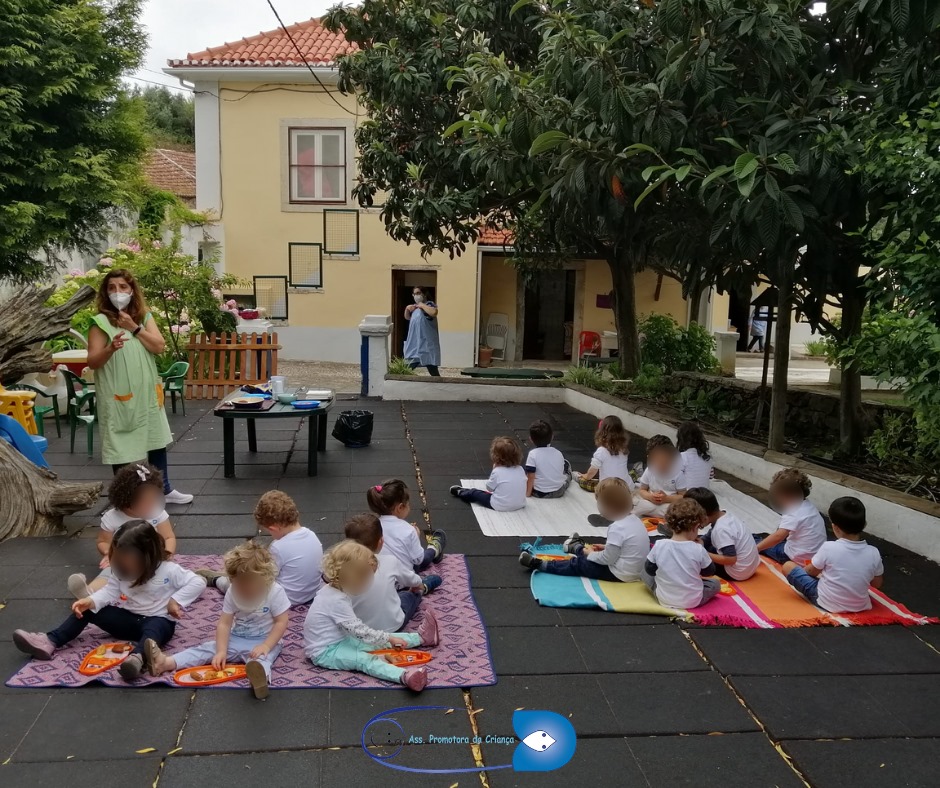 Preschool children sitting on the ground outdoors during a snack time.