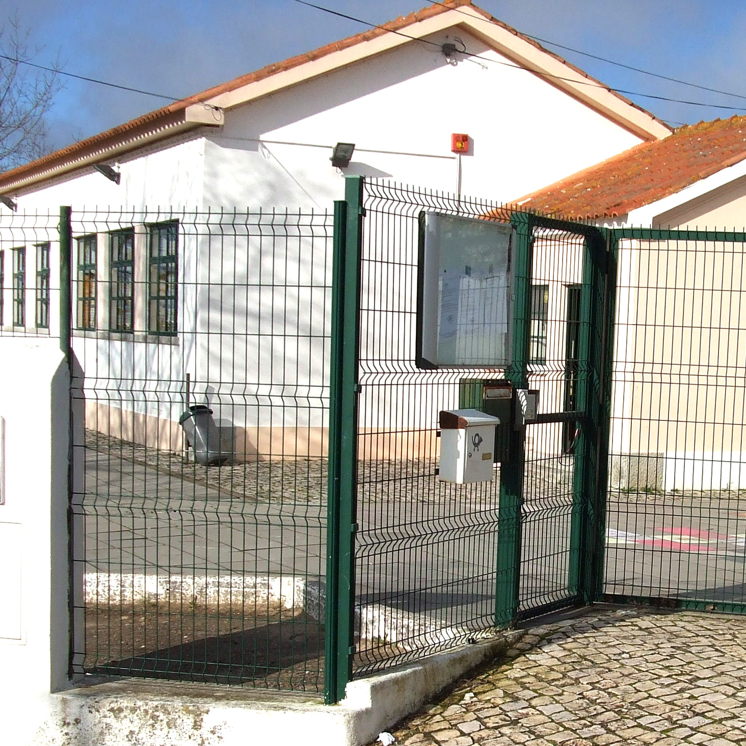Exterior view of Escola Básica e Secundária Alto dos Moinhos, showing a section of the school building behind a green metal fence.