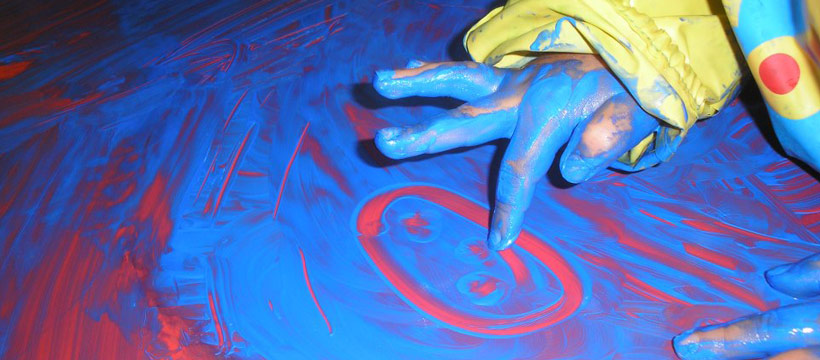 Child's hands covered in blue and red paint, creating artwork on a large surface.