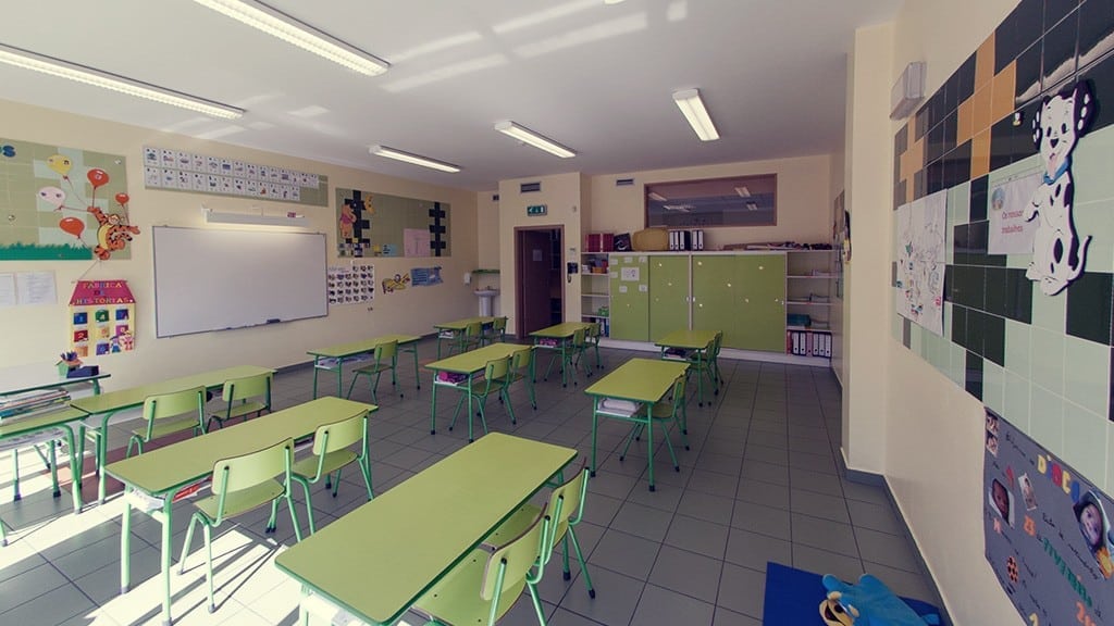 Preschool classroom with green tables and chairs, whiteboard, and educational materials on the walls