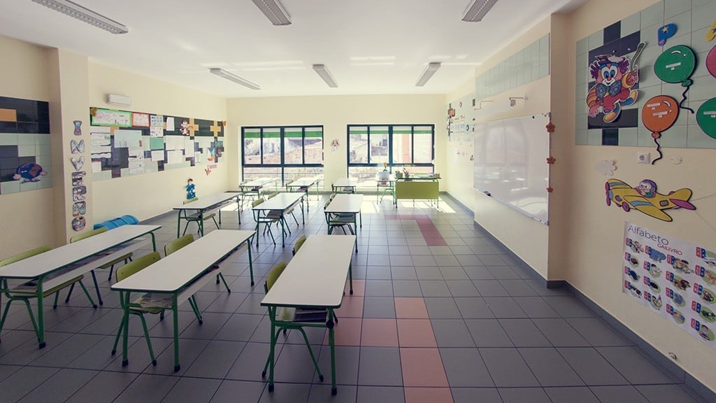 Preschool classroom with small tables and chairs, educational posters, and a whiteboard.