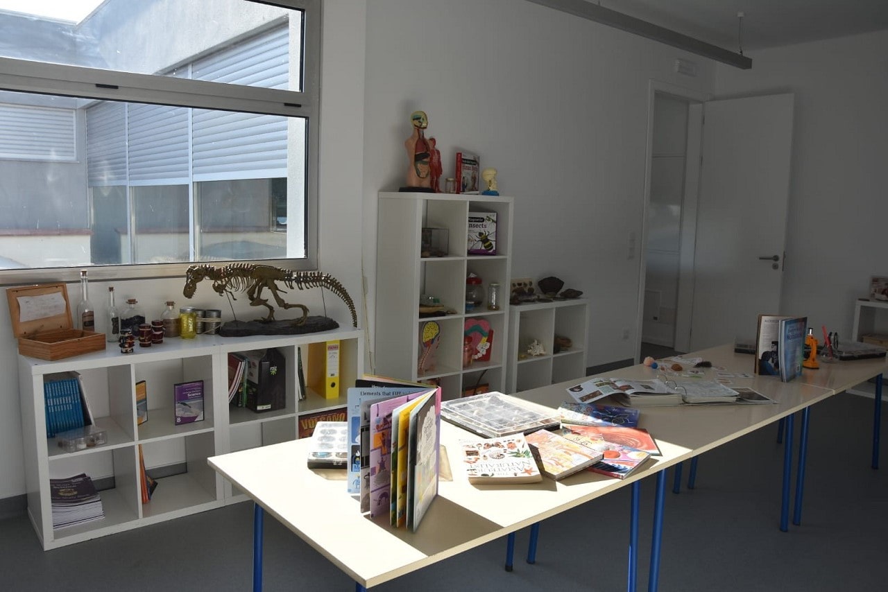 Preschool classroom with educational materials such as books, a dinosaur skeleton, and anatomical models.