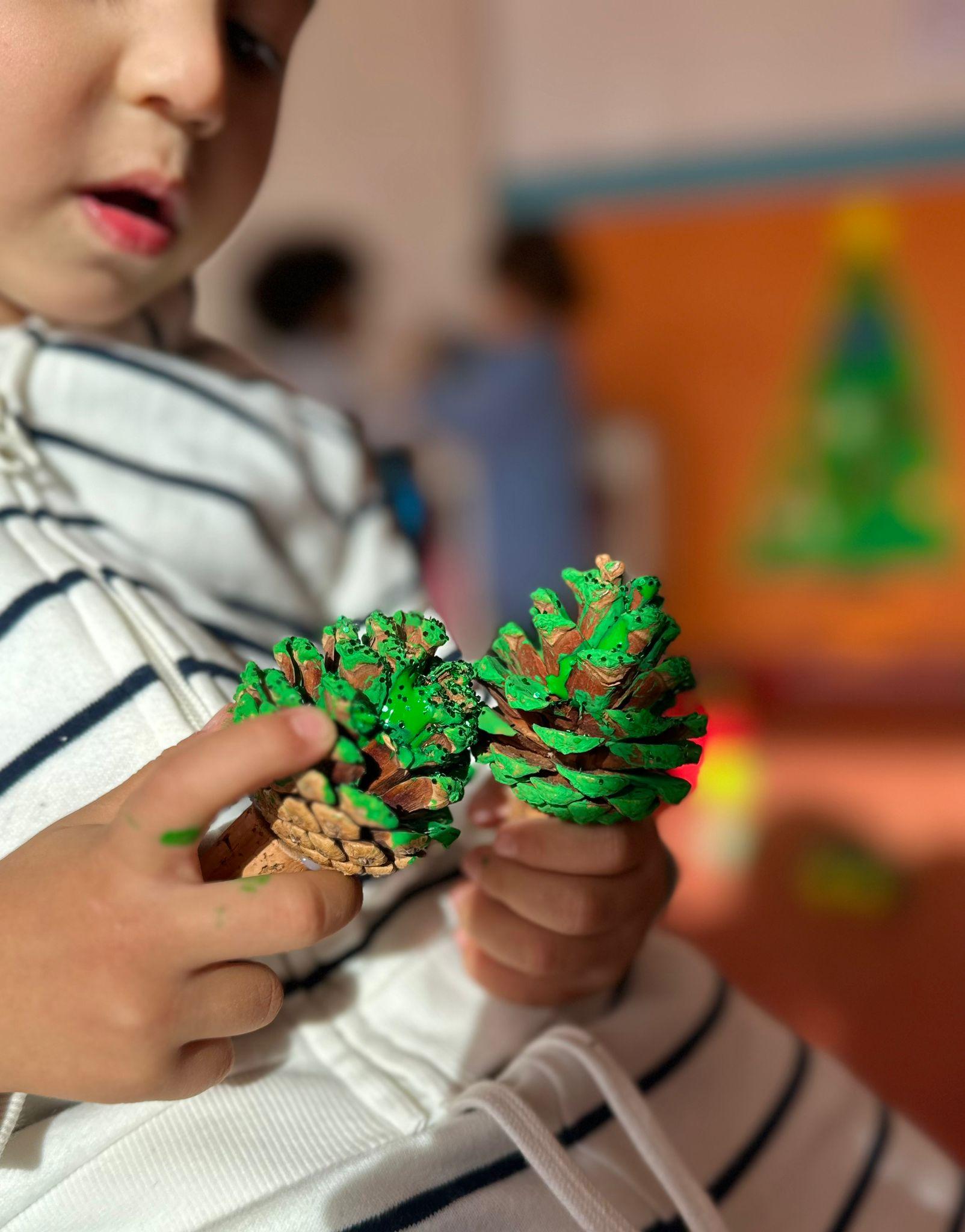 Preschool child painting pine cones green