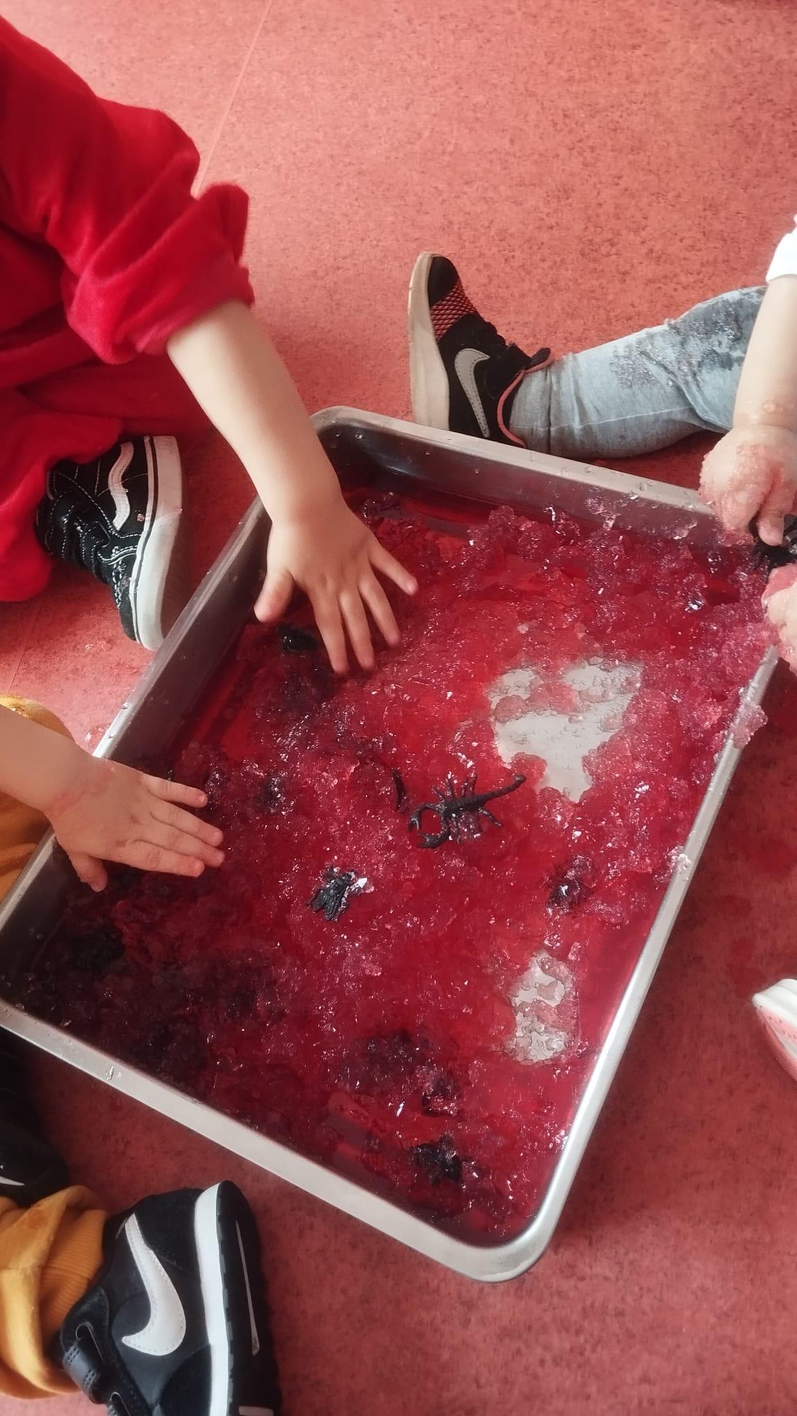 Preschool children exploring sensory play with red jelly and plastic insects