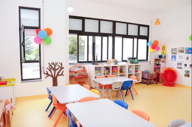 Preschool classroom with colorful tables and chairs, bookshelves, and learning materials
