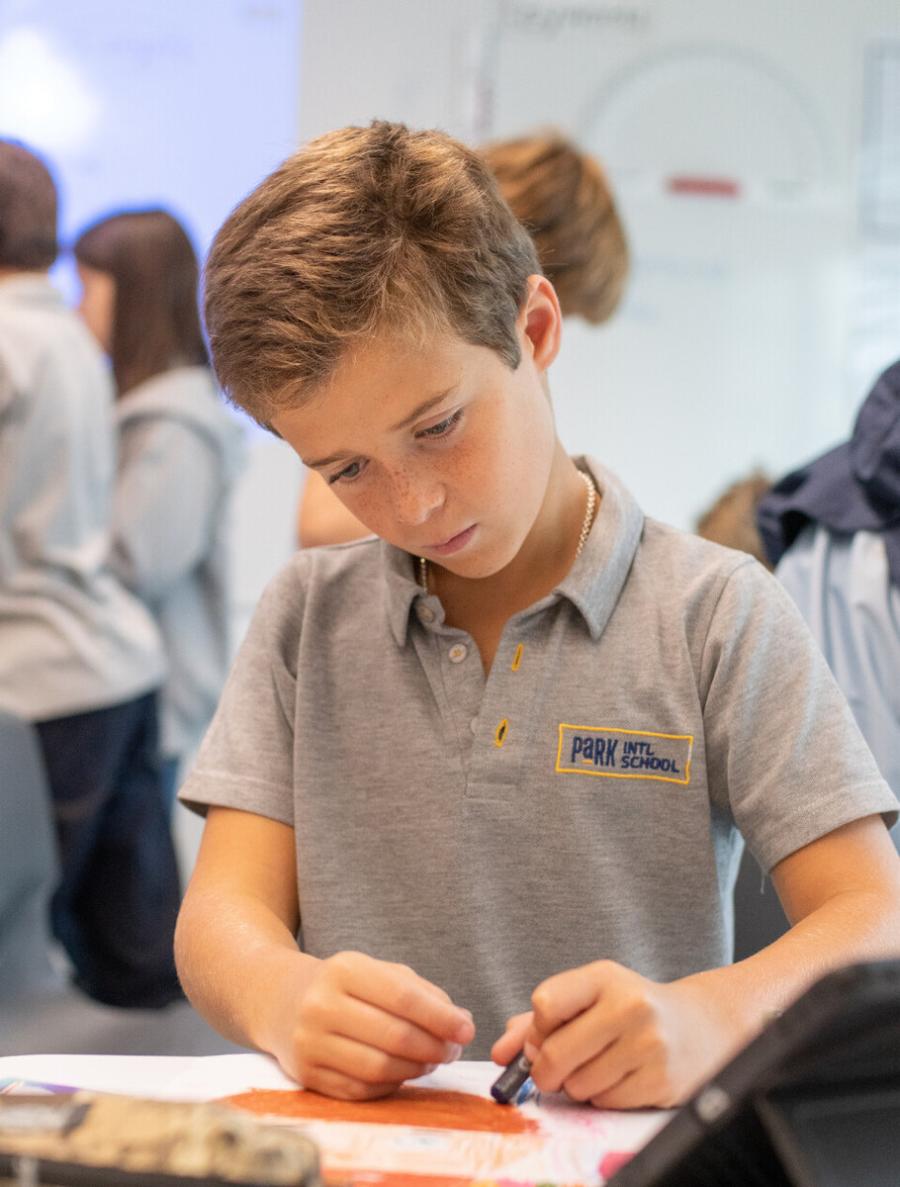 Student in gray polo shirt with school logo drawing