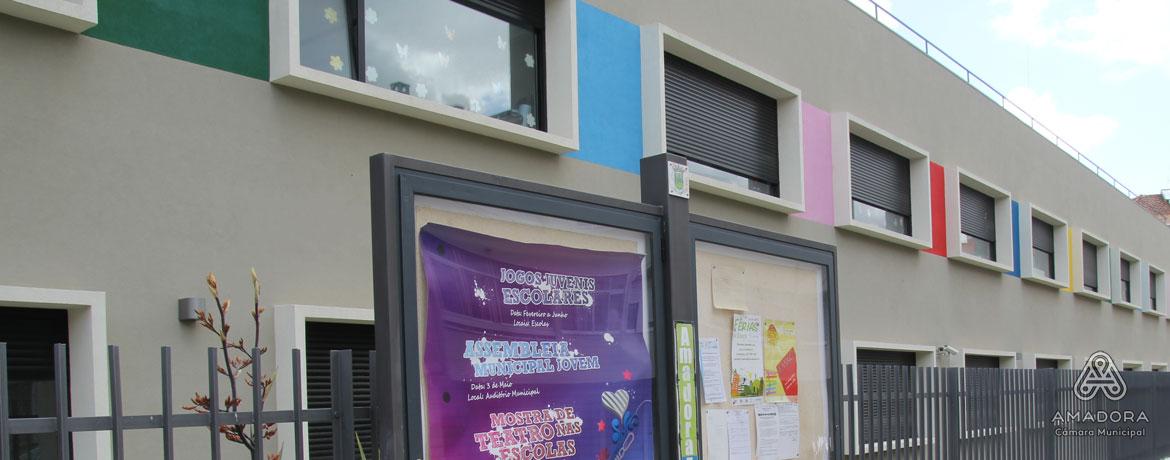 Exterior view of EB1\/JI\/Creche Aprígio Gomes preschool, showcasing its colorful building and a notice board with school event posters.