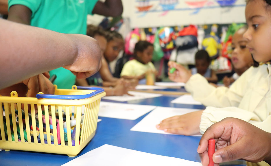 Preschool children participate in a colorful art and craft activity, using crayons from a basket.