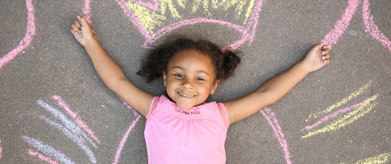 Happy preschool girl laying on the ground with colorful chalk drawings