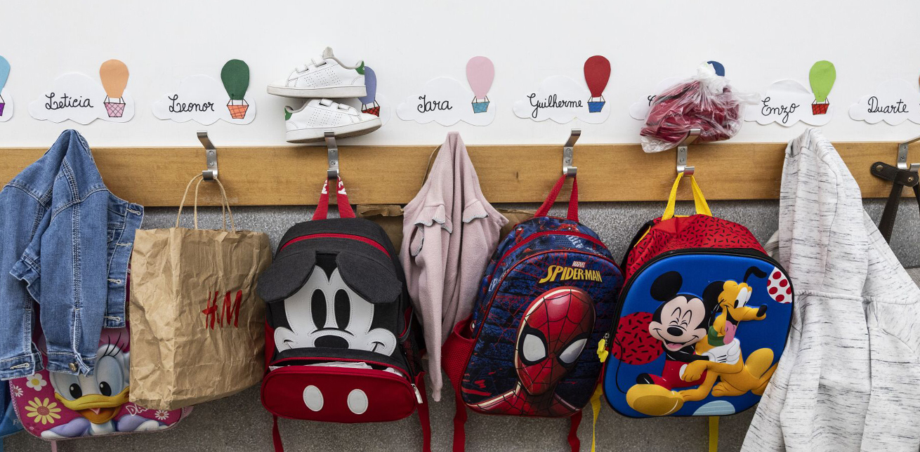 Backpacks and other belongings hang on hooks in a preschool classroom.