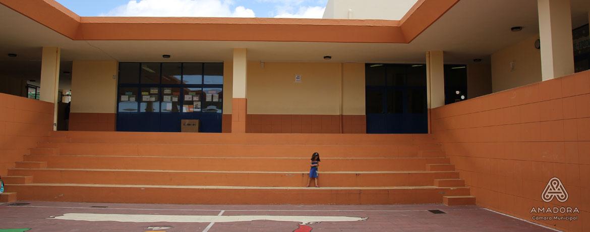 Exterior view of Jardim de Infância Cerrado da Bica preschool, showing a playground area with orange walls and a child standing on the steps.