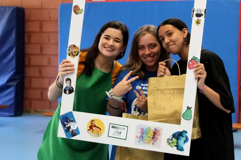 Three girls at an award ceremony holding a large photo frame with cartoon stickers