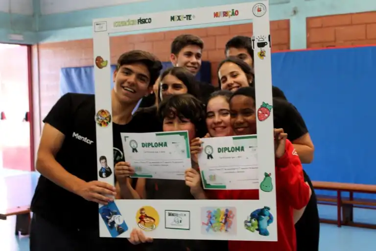 Students holding diplomas and smiling for a photo inside a decorated frame.